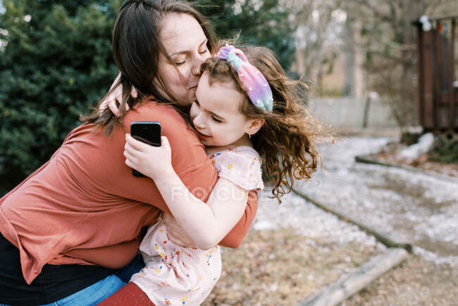 Uma mãe segurando e confortando sua filha segurando o telefone celular — Fotografia de Stock