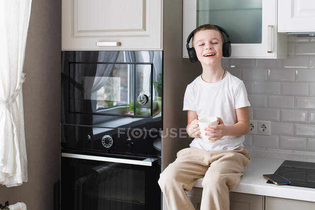 Мальчик слушает музыку с наушниками на кухне — стоковое фото