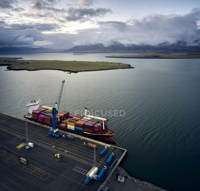 Вид беспилотника на загруженную баржу, пришвартованную на пристани в промышленном порту с мрачным небом и горами на заднем плане — стоковое фото