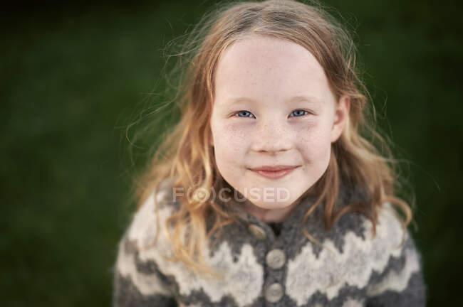 From above positive ginger girl with freckled face smiling and looking at camera while standing on green lawn — Stock Photo