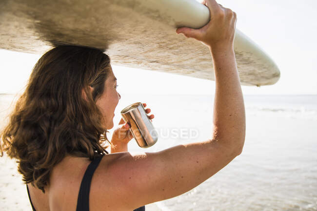 Surferin mit Brett trinkt Kaffee am Strand — Stockfoto