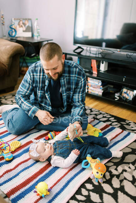 Um jovem pai feliz e sua filha bebê brincando juntos no chão — Fotografia de Stock