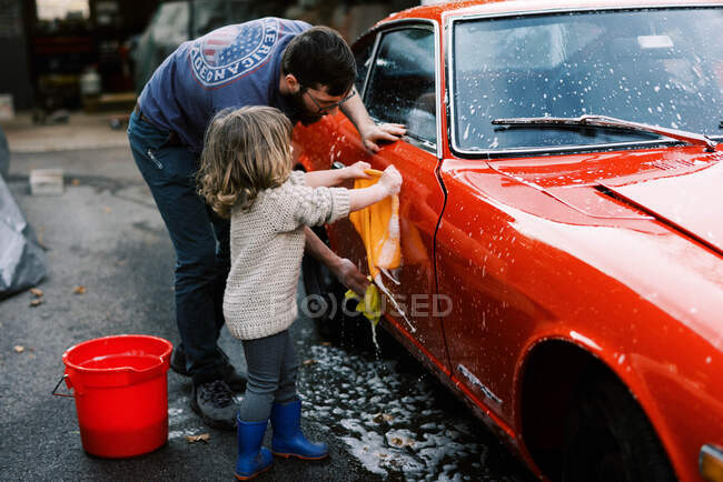Маленька дівчинка прибирає червону класичну машину разом з батьком — стокове фото