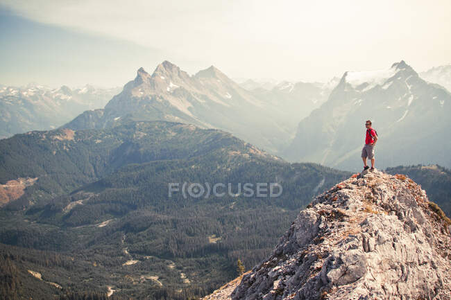 Mann in Rot steht auf Gipfel und blickt auf die Aussicht. — Stockfoto