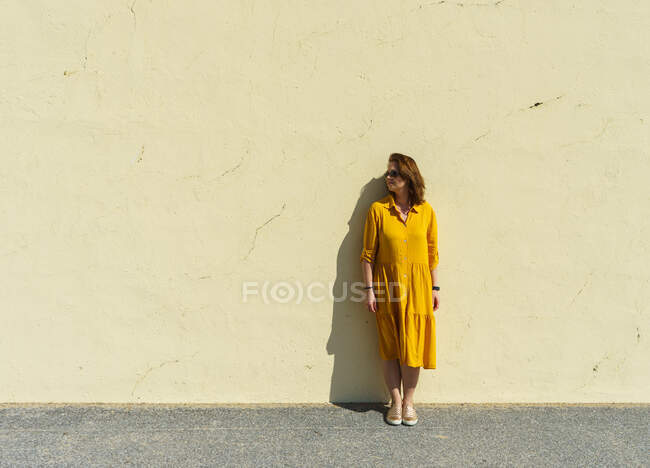 Young woman in a yellow dress and a white t-shirt on a background of a wall — Stock Photo