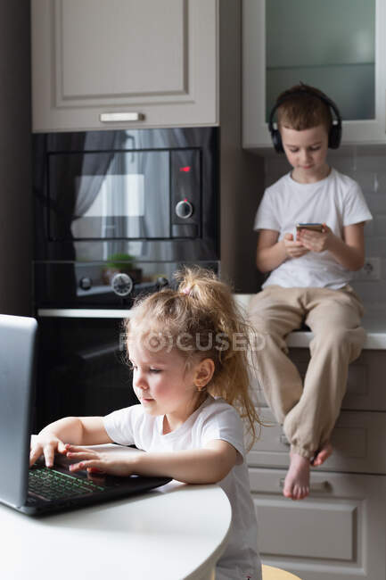 Niño escuchando música y hermana usando portátil - foto de stock