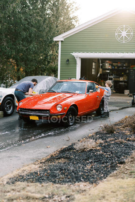Crianças pequenas ajudando seu pai a lavar um clássico carro vermelho velho lá fora — Fotografia de Stock