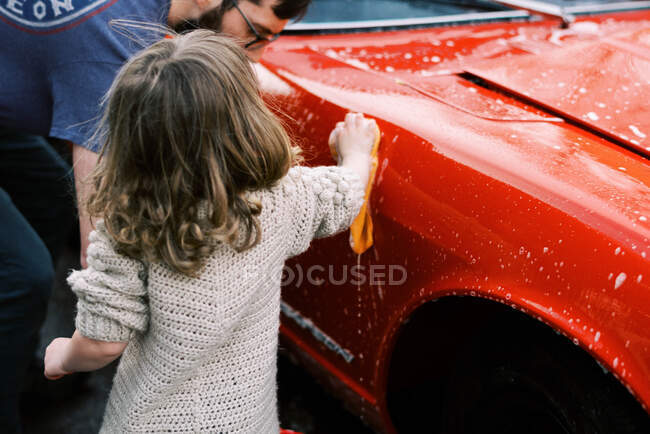 Kleines Mädchen putzt gemeinsam mit ihrem Vater einen roten Oldtimer — Stockfoto