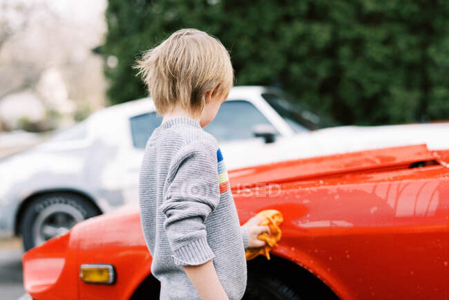 Niño en suéter lavando un coche clásico en primavera - foto de stock
