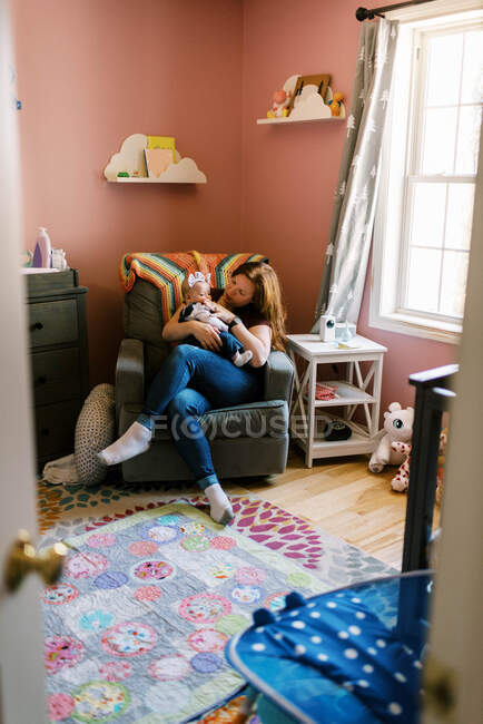 Eine Mutter sitzt im Schaukelstuhl im Kinderzimmer, während sie ihr Baby hält — Stockfoto
