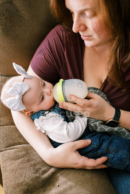 Uma mulher com cabelo vermelho alimentando sua filha bebê com uma garrafa — Fotografia de Stock