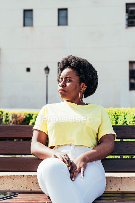 Портрет черной девушки с афроволосами и серьгами на кольце загорает на городской скамейке. — стоковое фото