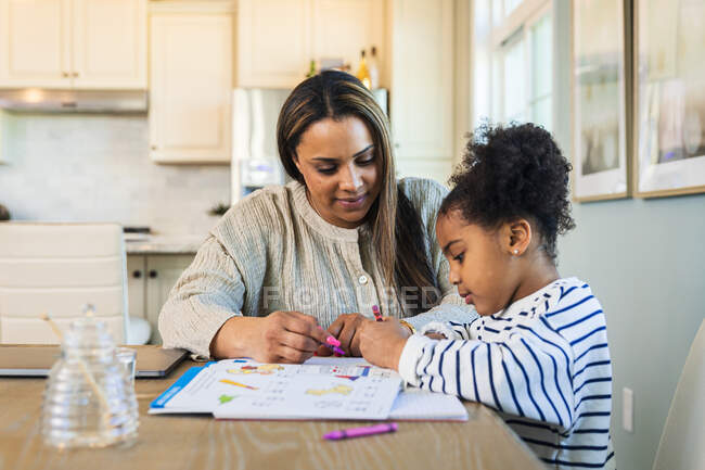 Madre enseñando linda hija sentada en la mesa - foto de stock