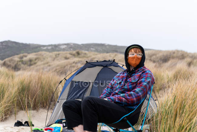 Людина сидить у кріслі в масці в похмурий день на пляжі — стокове фото