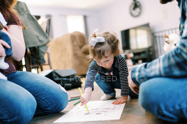 A little toddler girl coloring on the floor with her parents together — Stock Photo