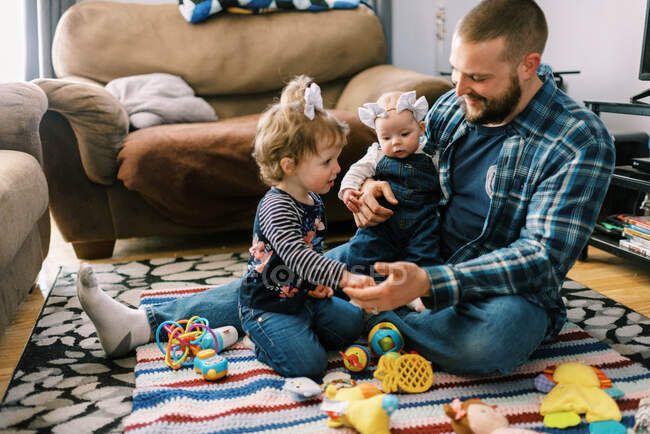 Ein junger Vater spielt mit seinen beiden Töchtern im Wohnzimmer — Stockfoto