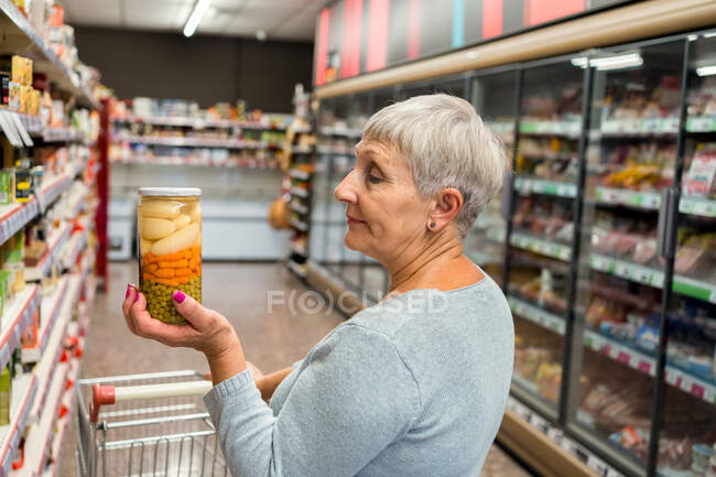 Взрослая белая женщина с овощным горшком в супермаркете — стоковое фото