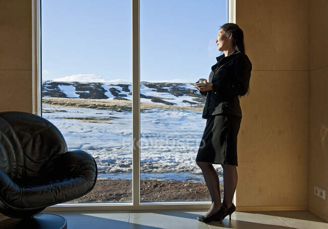 Женщина в деловой одежде, выглядывающая в окно из дома отдыха — стоковое фото