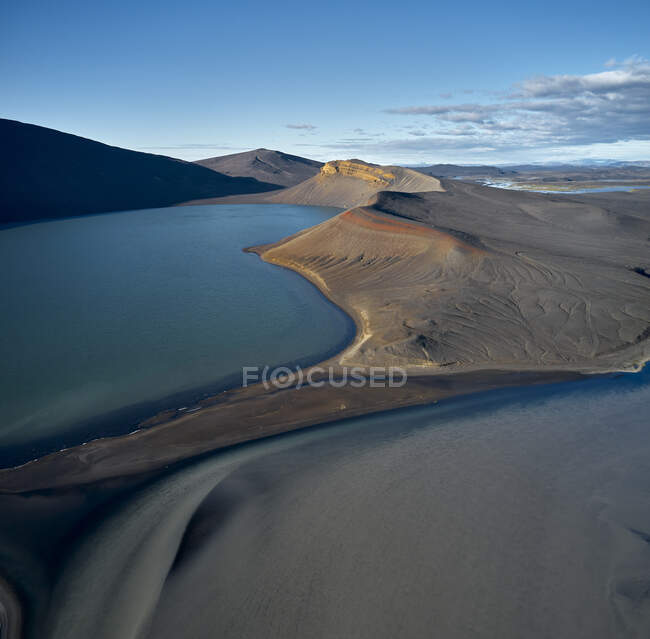 Lac paisible avec eau bleue situé dans un terrain gris vallonné contre ciel bleu nuageux — Photo de stock