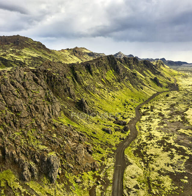 Vista aérea de montanhas localizadas perto de estrada e terreno seco em dia nublado na Islândia — Fotografia de Stock