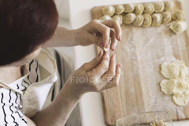 Eine Frau in einer weißen Küche bereitet traditionelle russische Knödel aus Fleisch und Teig zu — Stockfoto