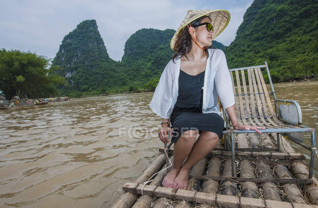 Donna in tradizionale asiatico seduta su zattera di bambù a Yangshuo — Foto stock