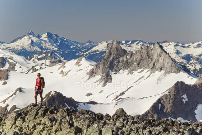 Young attractive backpacker stands on rocky ridge with mountain views — Stock Photo