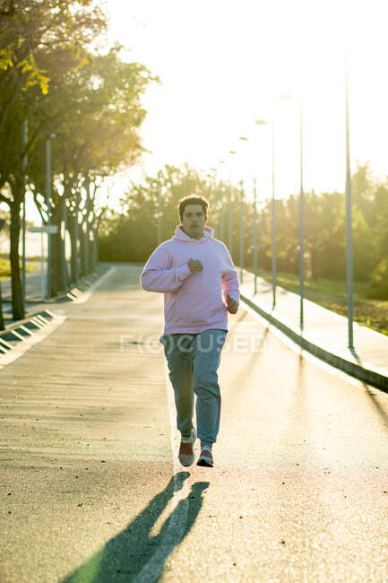 Fat man running down the center of a street with evening sun behind — Stock Photo