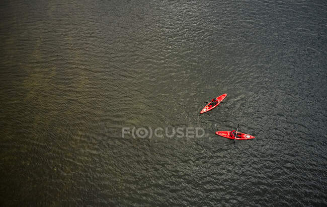 Drone vista di persone che cavalcano kayak rossi su increspatura acqua scura del lago in Islanda — Foto stock
