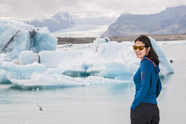 Mujer joven con una chaqueta blanca y gafas en un lago congelado. - foto de stock