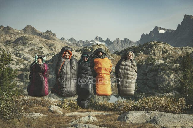 Unbekümmerte Freundinnen springen im Urlaub mit Schlafsäcken gegen Gebirge — Stockfoto