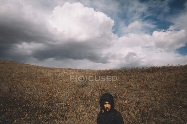 Uma menina de vestido preto em pé na areia em um fundo de céu nublado. — Fotografia de Stock