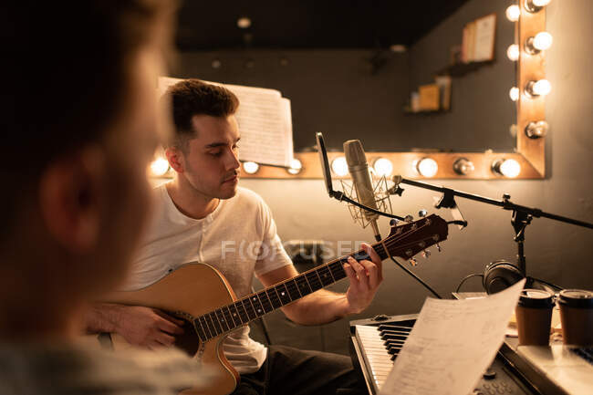 Musicista maschile che suona la chitarra vicino allo scrittore di canzoni mentre crea musica in studio — Foto stock