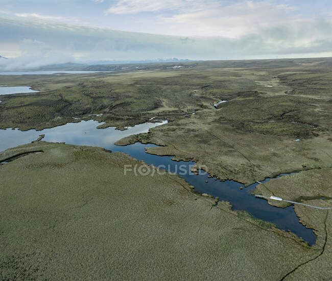 Drone view of plain terrain with lakes located against cloudy sky in countryside — Stock Photo