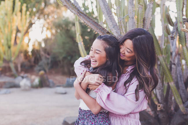 Asiática madre abrazando pre-adolescente hija y haciéndola reír. - foto de stock