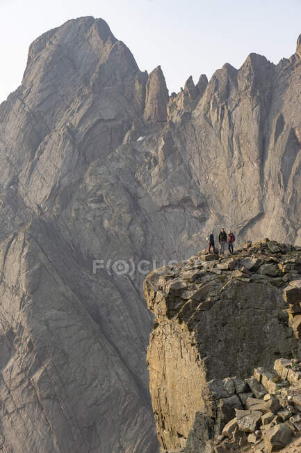 Hombre y mujeres de pie contra acantilado rocoso mientras mochileros en vacaciones - foto de stock