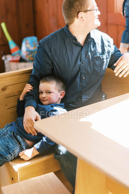 Un padre sosteniendo a su hijo en sus brazos mientras observa a su otro niño - foto de stock