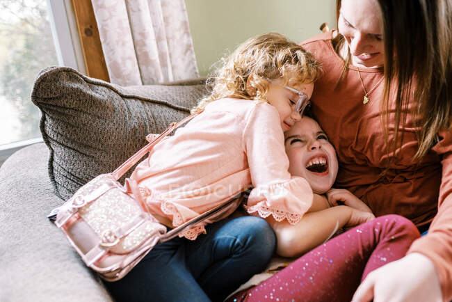 Two girls and their mother laughing together on couch — Stock Photo