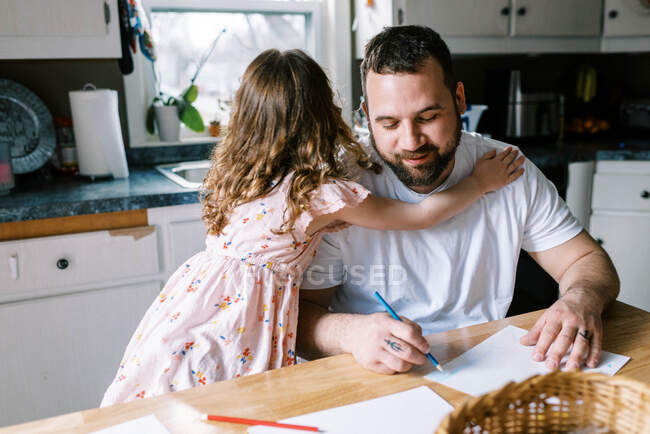 A father and his little daughter coloring together at kitchen table — Stock Photo