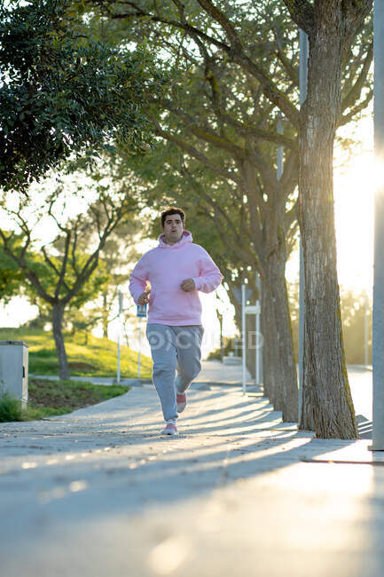 Gordo homem correndo pela calçada em um parque com luz do pôr do sol atrás — Fotografia de Stock