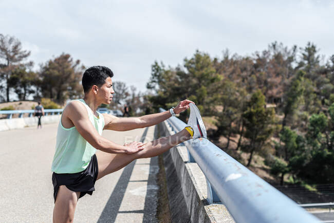 Corredor sul-americano esticando a perna depois de treinar em uma ponte urbana. Conceito de execução. — Fotografia de Stock