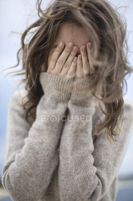 Das Mädchen lacht und bedeckt ihr Gesicht mit den Händen, der Wind entwickelt sich — Stockfoto
