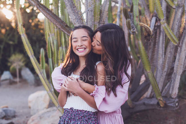 Asian mother kissing pre-teen daughter on the cheek. — Stock Photo