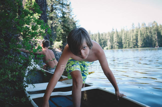 Junge in Shark Shorts steigt am Seeufer ins Kanu. Sommertag. — Stockfoto