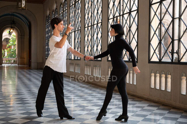 Hombre y mujer tomados de la mano mientras bailan juntos en el pasillo durante el ensayo - foto de stock