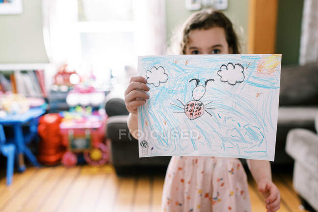 Гордая маленькая девочка, держащая в руках рисунок женщины-жука в своей комнате — стоковое фото