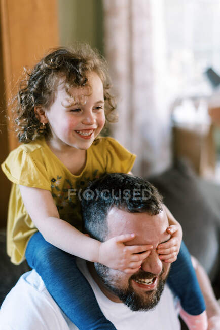 Um pai brincando com sua filha em seus ombros na sala de estar — Fotografia de Stock