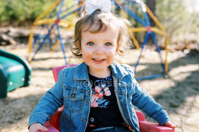 Pequeña niña con una gran sonrisa sentada en una silla de jardín de plástico - foto de stock