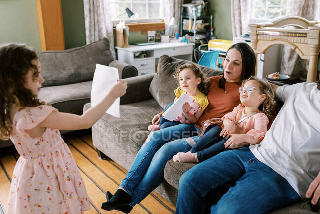 Маленькая гордая девочка показывает своей счастливой семье свой рисунок в гостиной — стоковое фото