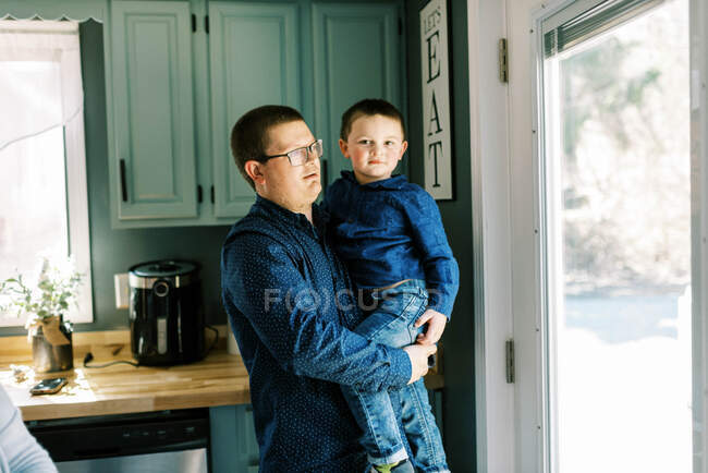 Un niño y su padre de pie juntos en la cocina mirando hacia fuera - foto de stock
